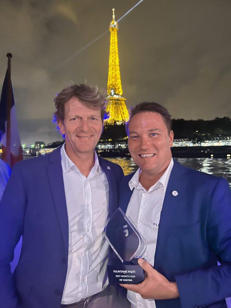 Jörg Stümke and John Rossbach together with the illuminated Eiffel Tower in the background. The man on the right, a successful boat dealer, is holding an award for his best growth. Both are wearing white shirts and blue jackets.